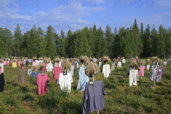 Artwork outdoor installation The silent people of Reijo Kela Straw dolls wear colorful clothes in a field at the edge of the forest, Suomussalmi, Kainuu, Finland