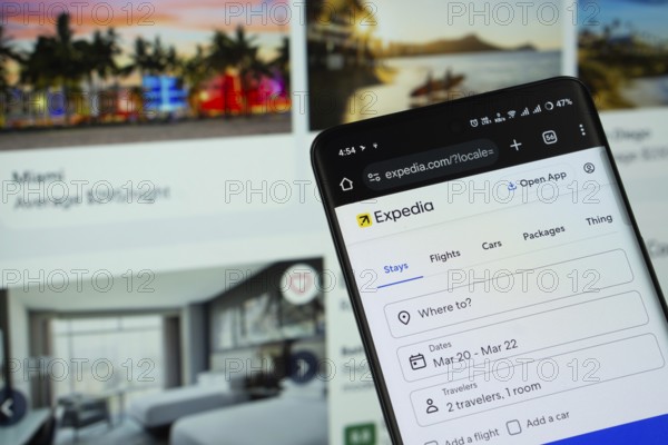 Dhaka, Bangladesh- 11 March 2025: Expedia logo is seen on a smartphone, with the website visible on a computer screen in the background