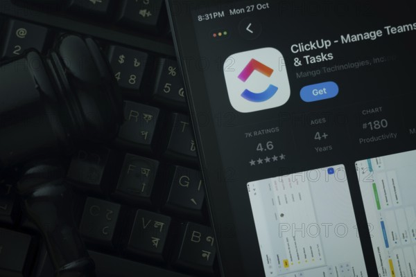 Dhaka, Bangladesh- 28 Oct 2025: An iPad displaying the ClickUp app against a judge's gavel and dark keyboard background