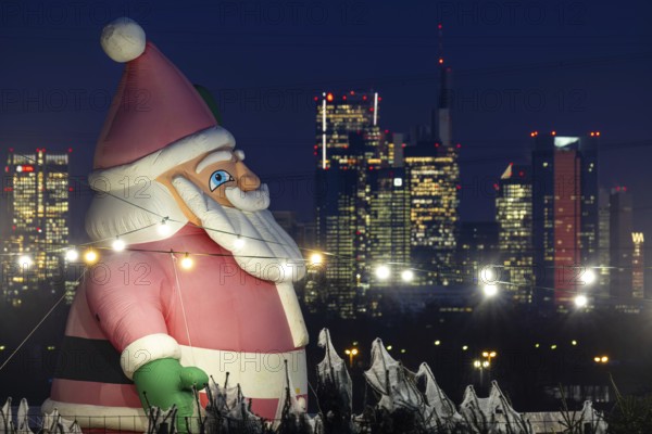 In a Christmas tree center near Frankfurt am Main, a multi-metre-high inflated figure of Santa Claus rises in front of the glowing banking skyline, Frankfurt am Main, Hesse, Germany