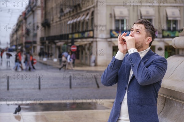 Man musician in a blue blazer and white sweater playing blues on a harmonica with eyes closed, standing outdoors in city street