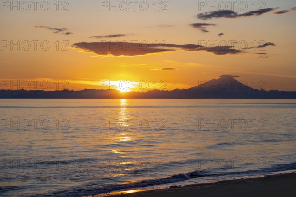 View of Cook Inlet on white mountain peaks of Mount Redoubt at sunset, picturesque golden light of the midnight sun, mountains of the Aleutian Range, Anchor Point, Anchor River State Recreation Area, Alaska, USA
