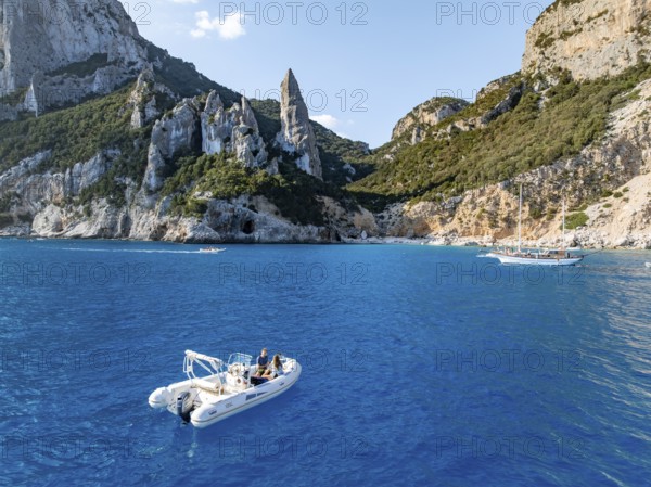 Motor boat off picturesque rocky coast, cliffs with L'Aguglia pinnacle, blue sea and Cala Goloritzé beach, aerial view, Golfo di Orosei, Baunei, Sardinia, Italy