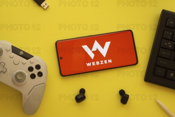 Dhaka, Bangladesh- 22 Mar 2025: Smartphone with Webzen logo, game controller, and earbuds on a background