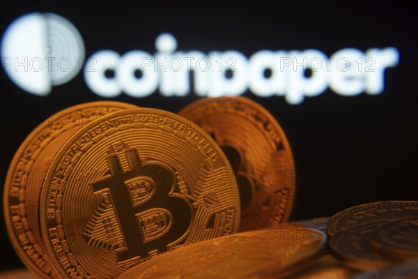 Dhaka, Bangladesh- 19 Sep 2025: Close-up of Bitcoin coins with the Coinpaper logo visible on a screen in the background
