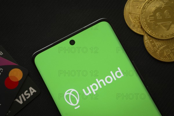 Dhaka, Bangladesh- 03 Sep 2025: Smartphone displaying Uphold logo surrounded by Bitcoin coins and payment cards