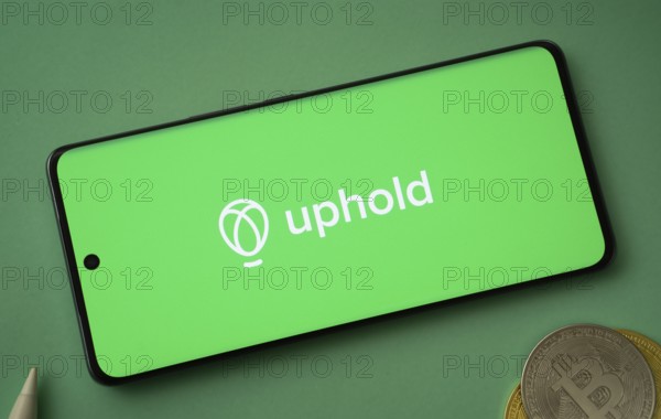 Dhaka, Bangladesh- 19 Sep 2025: Uphold logo on smartphone screen near Bitcoin coin and QR code on background