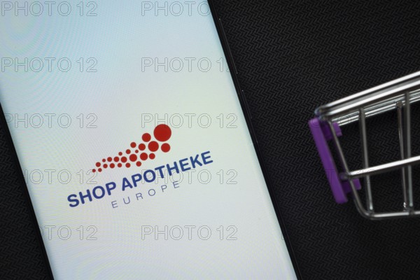 Dhaka, Bangladesh- 21 Nov 2025: A smartphone displaying the Shop Apotheke logo next to a miniature shopping cart on a background