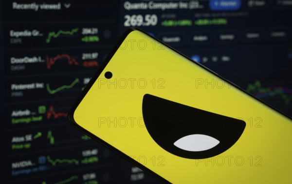 Dhaka, Bangladesh- 18 March 2025: Yubo logo is displayed on a smartphone screen, with a stock graph webpage visible on a computer screen in the background