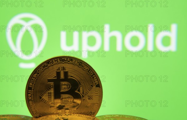Dhaka, Bangladesh- 19 Sep 2025: Close-up of Bitcoin coins with the Uphold logo visible on a screen in the background