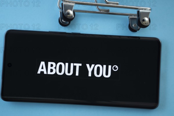Dhaka, Bangladesh- 21 Nov 2025: Smartphone screen showing the About You logo with shopping cart wheels on a blue background