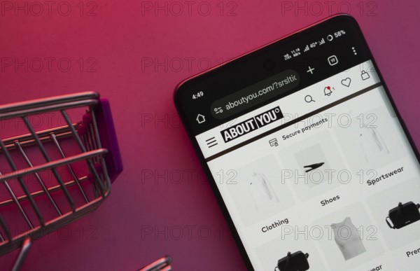 Dhaka, Bangladesh- 21 Nov 2025: A smartphone displaying the About You website with a shopping cart is shown on a vibrant background