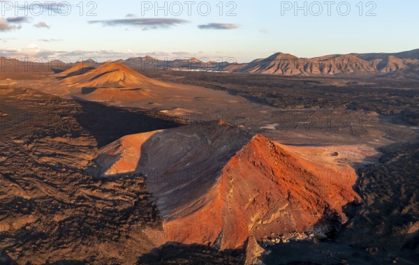 Picturesque volcanic landscape in evening light, red volcano Montaña Bermeja between lava fields, aerial view, Lanzarote, Canary Islands, Spain