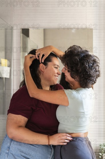 A lesbian couple shares a morning routine in the bathroom, styling hair, creating a candid and intimate moment