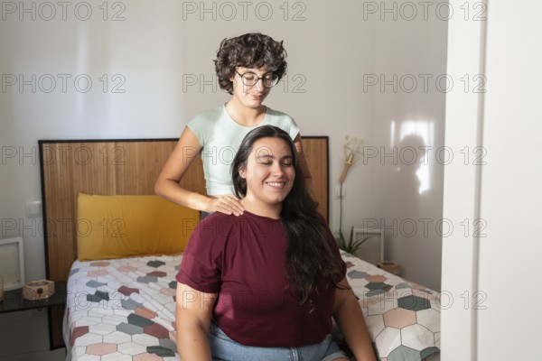 A loving lesbian couple sharing a peaceful moment in a cozy bedroom, with one partner gently massaging the other's shoulders, creating a serene and intimate atmosphere