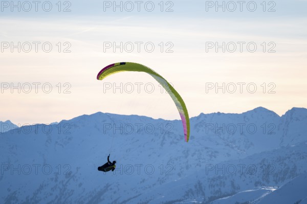 Paragliders flying over snowy mountain peaks in winter in evening light, Kitzbühel Alps, Tyrol, Austria