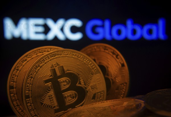 Dhaka, Bangladesh- 03 Sep 2025: Close-up of Bitcoin coins with the MEXC Global logo visible on a screen in the background