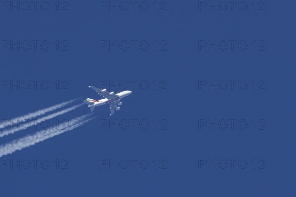 Airbus A380 jet passenger aircraft of Emirates airlines flying in a blue sky with contrails or vapour trails behind, England, United Kingdom