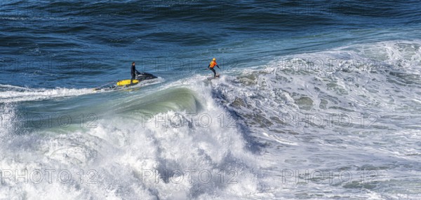 Surfers with their jet ski pilots in the Atlantic waves below Farol de Nazaré, Forte São Miguel, known as a surfer hot spot with monster waves between November and February of each year, Nazaré, Portugal