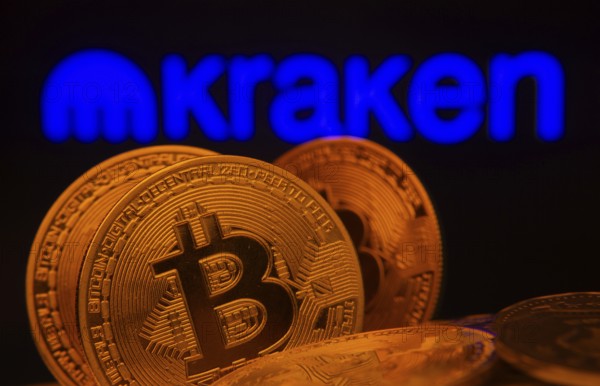 Dhaka, Bangladesh- 01 Nov 2025: Close-up of Bitcoin coins with the Kraken logo visible on a screen in the background