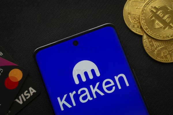Dhaka, Bangladesh- 26 Aug 2025: Smartphone displaying Kraken logo surrounded by Bitcoin coins and payment cards