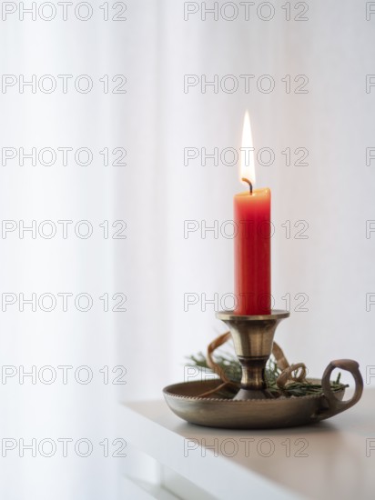 Red candle burning on a brass candlestick decorated with tree branch