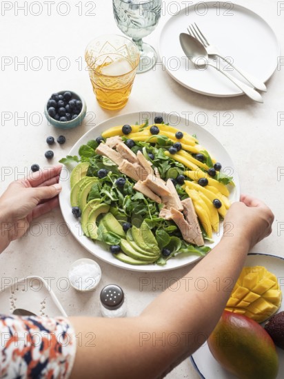Woman placing a plate of healthy tuna, mango, avocado and blueberry salad on a table
