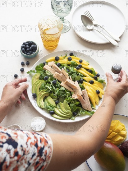 Woman seasoning a colorful healthy salad with chicken, mango, avocado, blueberries and lamb's lettuce