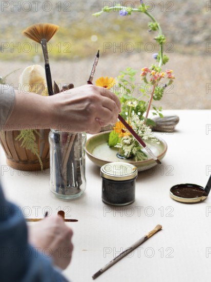 Florist creating ikebana arrangement, painting kenzan and arranging flowers on a table