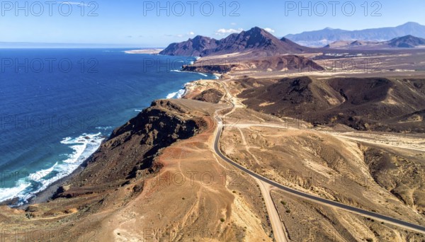 Desert landscape converges with ocean along a rugged coastal area, shore break at cliffs, blue cloudy sky at sunset, dry landscape in an aerial drone view, AI generated