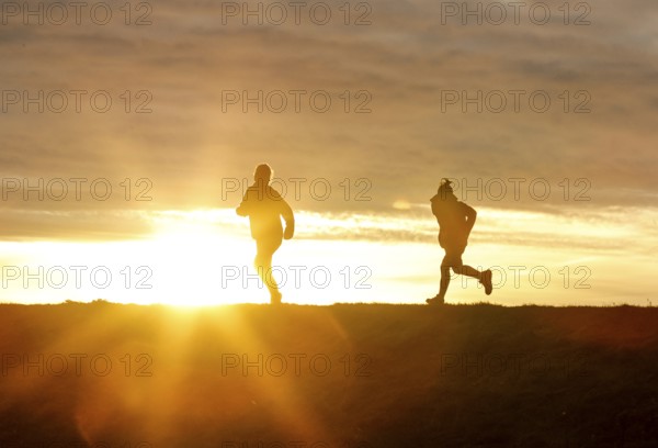 Woman and child walk across a dike on the island of Fehmarn at sunset, 13.10.2025, Fehmarn, Schleswig-Holstein, Germany