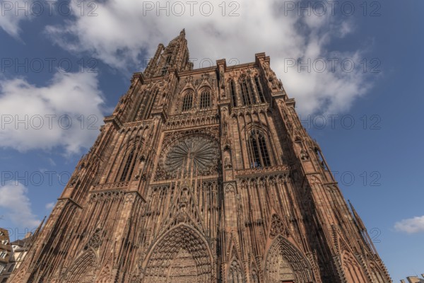 Strasbourg's Notre Dame Cathedral stands majestically there. Its magnificent architectural details are clearly visible under the blue, cloudy sky. Bas Rhin, Alsace, France