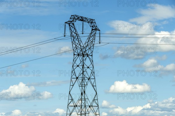 High voltage power lines against a bright blue sky with scattered clouds, Puy de Dome, Auvergne Rhone Alpes, France