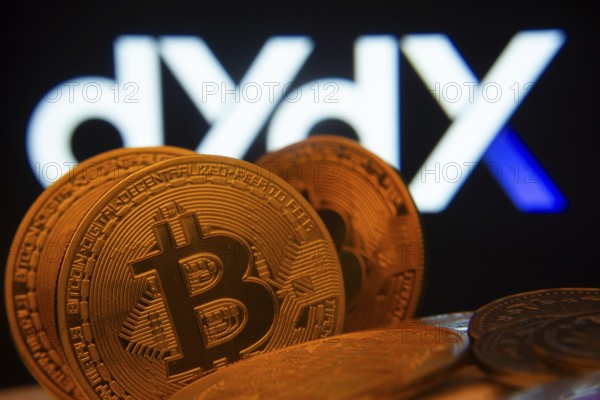 Dhaka, Bangladesh- 03 Oct 2025: Close-up of Bitcoin coins with the Dydx logo visible on a screen in the background
