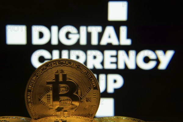 Dhaka, Bangladesh- 03 Oct 2025: Close-up of Bitcoin coins with the Digital currency group logo visible on a screen in the background