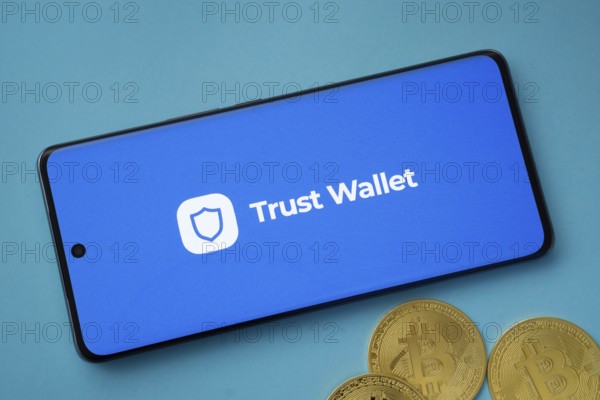 Dhaka, Bangladesh- 30 Sep 2025: Trust Wallet logo on smartphone screen near Bitcoin coin and QR code on blue background