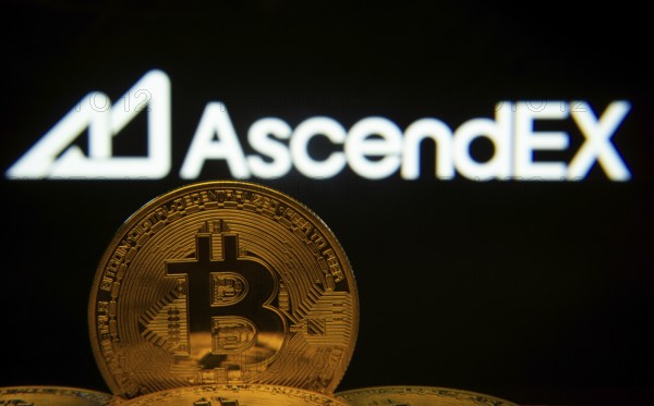 Dhaka, Bangladesh- 02 June 2025: Close-up of Bitcoin coins with the AscendEX logo visible on a screen in the background
