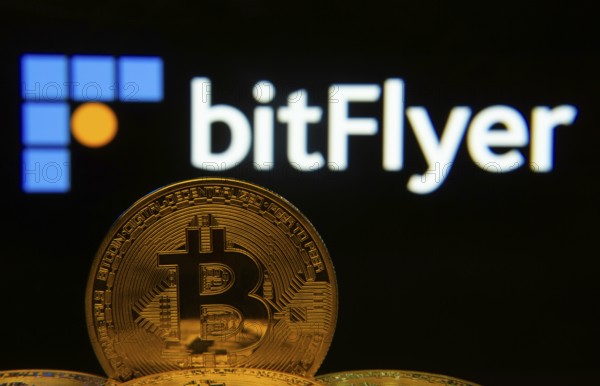 Dhaka, Bangladesh- 02 June 2025: Close-up of Bitcoin coins with the Bitflyer logo visible on a screen in the background