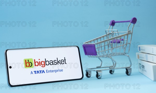 Dhaka, Bangladesh- 03 July 2025: Smartphone with BigBasket logo next to a small shopping cart and boxes against a blue background