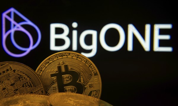 Dhaka, Bangladesh- 15 June 2025: Close-up of Bitcoin coins with the Bigone logo visible on a screen in the background