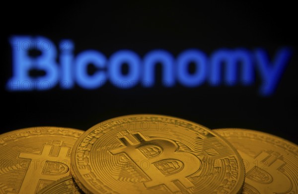 Dhaka, Bangladesh- 02 June 2025: Close-up of Bitcoin coins with the Biconomy logo visible on a screen in the background