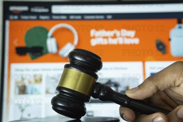 Dhaka, Bangladesh- 20 June 2025: A hand holds a gavel in front of a computer screen displaying Amazon's website