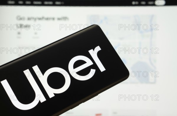 Dhaka, Bangladesh - 18 March 2025: The logo of the Uber is displayed on a smartphone screen, and the website Uber is visible on a computer screen in the background