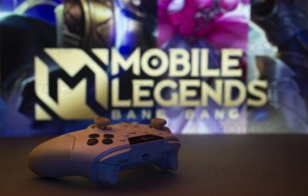 Dhaka, Bangladesh- 25 Aug 2025: A close-up of a white gamepad with Mobile Legends Bang Bang seen on screen in the background