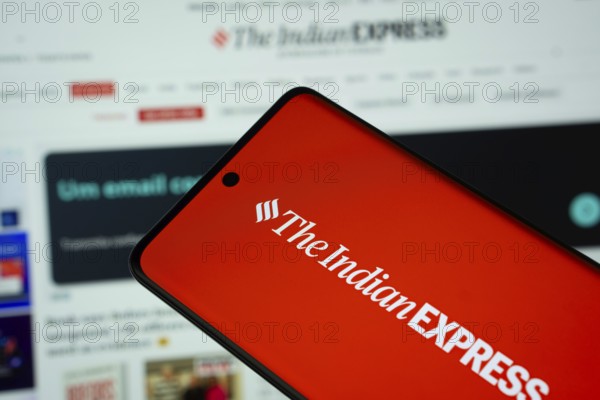 Dhaka, Bangladesh - 18 March 2025: The logo of The Indian Express is displayed on a smartphone screen, and the website is visible on a computer screen in the background