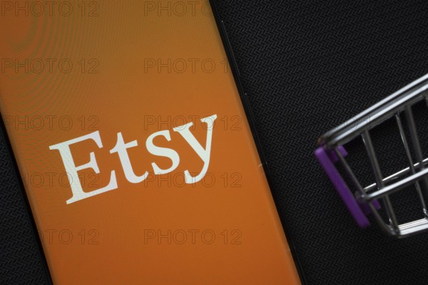 Dhaka, Bangladesh- 03 July 2025: A smartphone displaying the Etsy logo next to a miniature shopping cart on a background