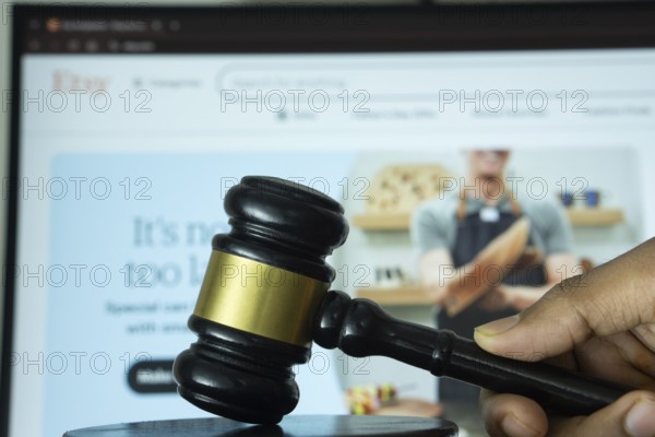Dhaka, Bangladesh- 20 June 2025: A hand holds a gavel in front of a computer screen displaying Etsy's website
