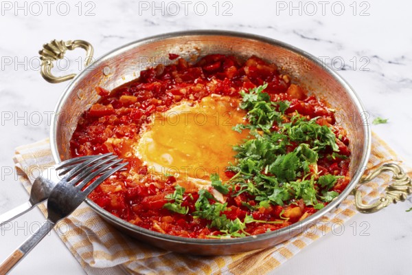 Traditional Turkish dish, scrambled eggs with tomatoes, Menemen, with herbs, in a frying pan, close-up, no people