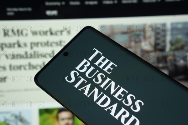 Dhaka, Bangladesh - 18 March 2025: The logo of The Business standard is displayed on a smartphone screen, and the website is visible on a computer screen in the background