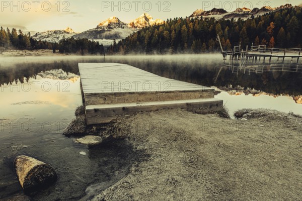 Lake Staz near Sankt Moritz in the Engadin in Switzerland. Morning atmosphere with fog in autumn. Water reflection and snow-covered mountains in the background